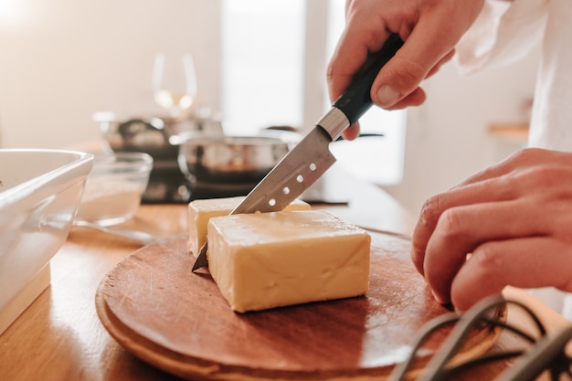 Unrecognizable person at home cutting a piece of butter on a board to continue cooking