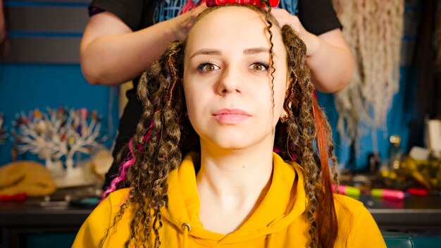 Unrecognizable person makes hairstyle for young woman in salon