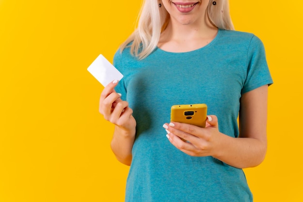 Unrecognizable person in an online payment with the card on the phone studio yellow background