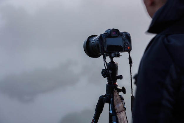 Unrecognizable photographer shooting misty outdoor scene with contemporary black digital camera on a tripod