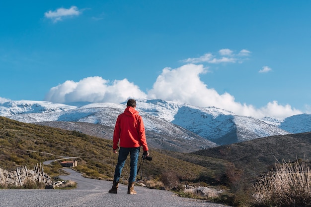 Unrecognizable photographer standing in the middle of a road looking at the snowy mountains