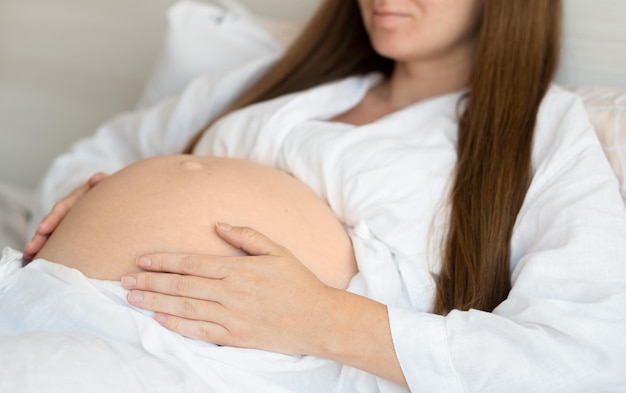 집에서 침대에 누워 알아볼 수 없는 임신한 여성 애무스트로킹 배 아기 범프잘린 클로즈업 샷행복한 아름다운 임신미래의 자식 개념에 대한 사랑
