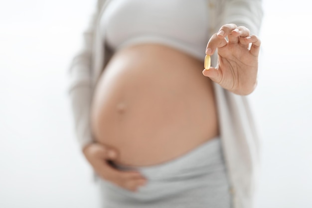 Unrecognizable pregnant woman showing pills white background
