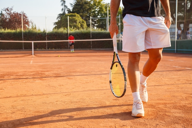 Unrecognizable professional tennis player walking on tennis court on sunny day.  