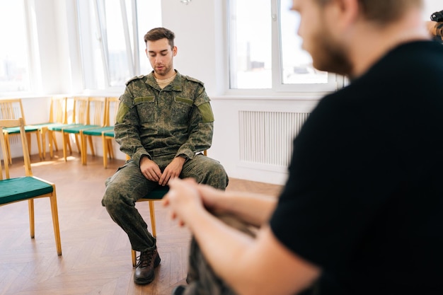 unrecognizable psychologist talking to group of male veterans in camouflage uniform sitting in