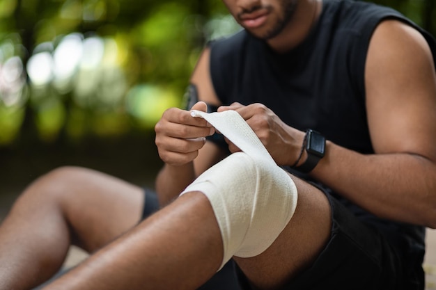 Photo unrecognizable sportsman sitting on the ground wrapping injured knee