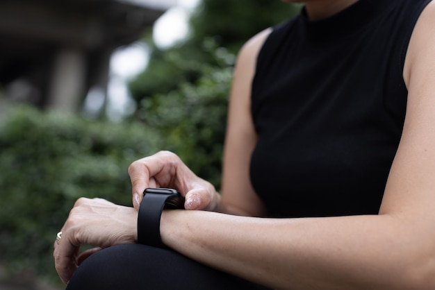 Le donne sportive irriconoscibili in abbigliamento sportivo alzano la mano e usano il dito per regolare l'impostazione dell'applicazione nello smartwatch al polso per controllare il risultato dopo l'allenamento o l'esercizio. concetto di buona assistenza sanitaria.