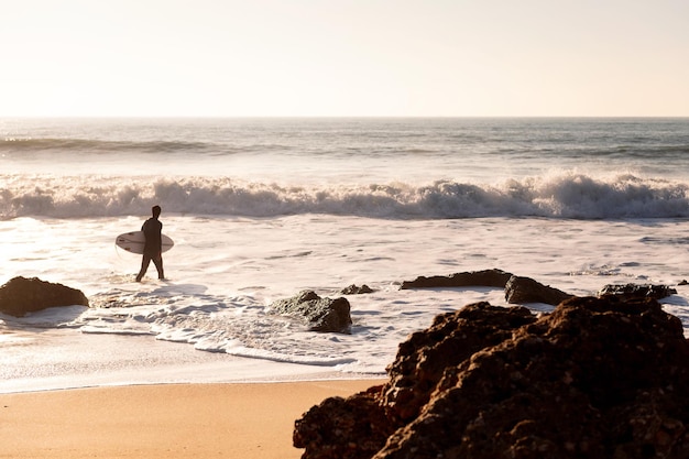 Unrecognizable surfer walking along the shore of the beach with his board under his arm at sunset concept of leisure and relax copy space for text