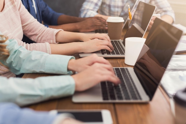 Unrecognizable team of young programmers working in software developing company, typing on laptops, testing new games or apps, copy space