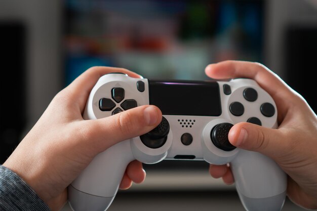 Unrecognizable teenage boy child sitting at home holding white gaming controller playing videogames on console station