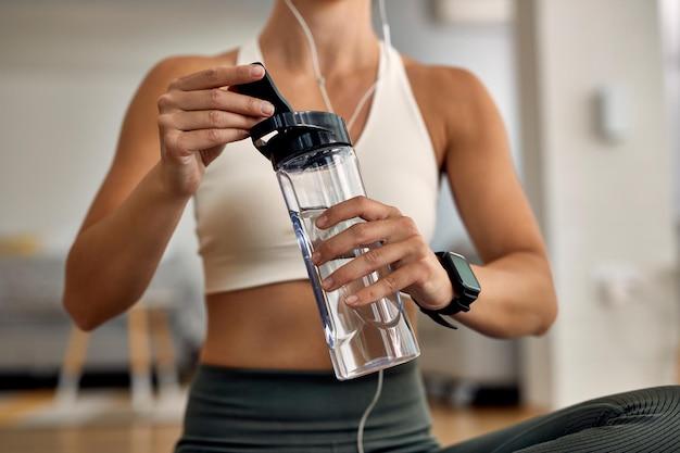 Неузнаваемая жаждущая спортивная женщина, использующая бутылку с водой во время тренировки в гостиной