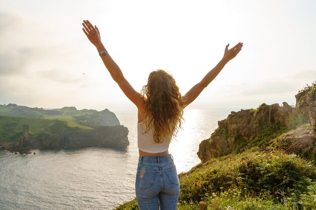 Foto donna irriconoscibile in una scogliera. vista orizzontale della donna caucasica da dietro che respira con le braccia spalancate