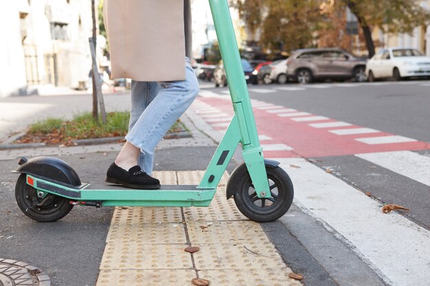 Unrecognizable woman crossing street with electric scooter in the city