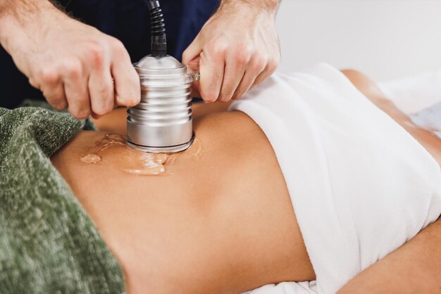 Foto donna irriconoscibile che riceve un trattamento di cavitazione ad ultrasuoni per la riduzione del grasso sull'addome presso il salone di bellezza.