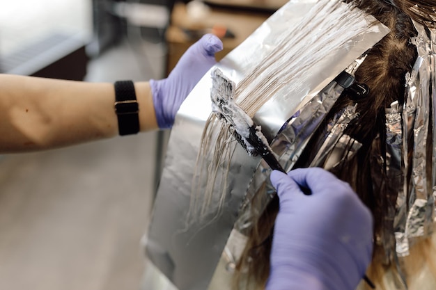 Unrecognizable woman hairdresser colorist holding dyed long hair on foil applying hair color with br