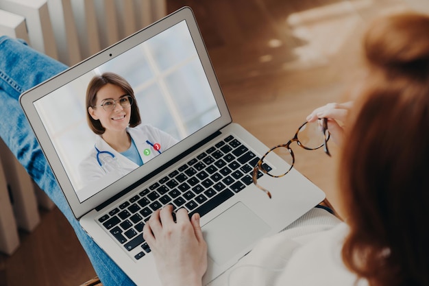 Foto una donna irriconoscibile ha una chat video con un medico esperto su un computer portatile riceve consulenza durante la quarantena discute il trattamento della malattia videochat con il medico generico retrovisione posteriore