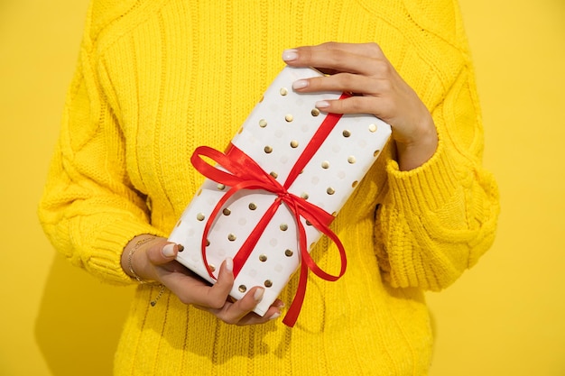 Unrecognizable Woman holding in hand present, gift box on yellow background