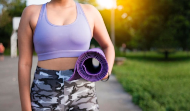 Unrecognizable woman holding a mat in the park Athlete woman's hands carrying the mat after exercising Fitness woman concept carrying yoga mat with copy space