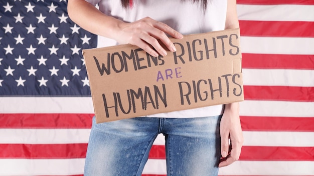 Unrecognizable woman is holding placard with sign Womens rights are human rights US flag