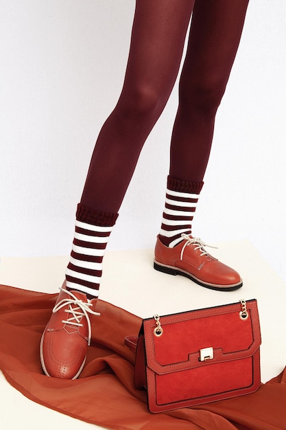 Unrecognizable woman legs wearing retro brown classic shoes, leggins and stripped socks. Stylish  accessory velvet clutch. Fashion vintage shop concept