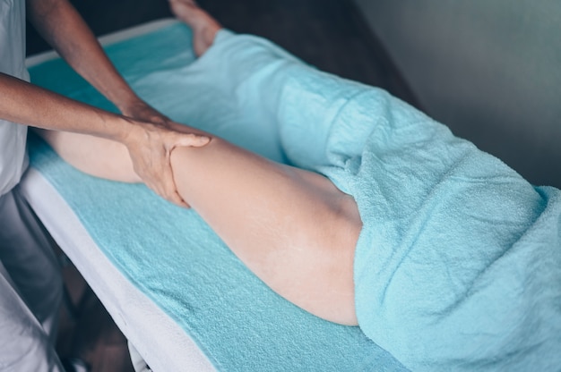 Photo unrecognizable woman lying on massage table and enjoying therapeutic massage. hands masseur therapist doing anti-cellulite massage in spa clinic.