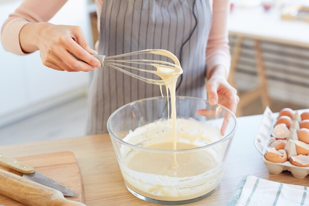 Unrecognizable woman making dough for cupcakes using whip, horizontal high angle shot