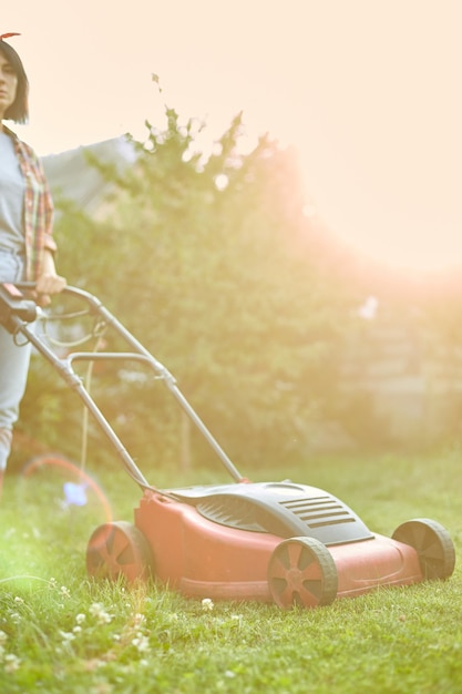 Photo unrecognizable  woman mows the lawn with a lawn mower grass at home garden, gardener woman working, beautiful summer landscape, sunlight, great design for any purposes, gardening concept