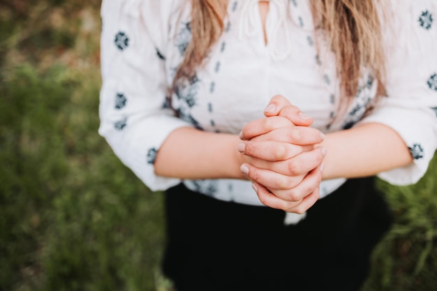 Unrecognizable woman outside praying on her knees with her hands together. Selective focus