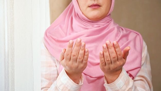 Una donna irriconoscibile in hijab rosa legge una preghiera mentre si tiene per mano di fronte a lei.