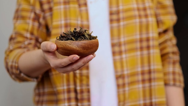 Unrecognizable woman in a plaid shirt holds a wooden bowl and dried seaweed in her hands