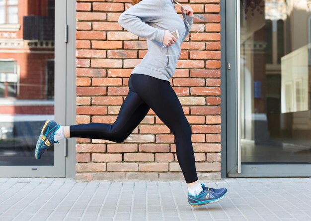 Unrecognizable woman running in city near brick building with mirror windows, copy space, side view