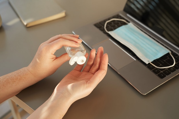 unrecognizable woman sanitizing hands while working at desk in post pandemic office