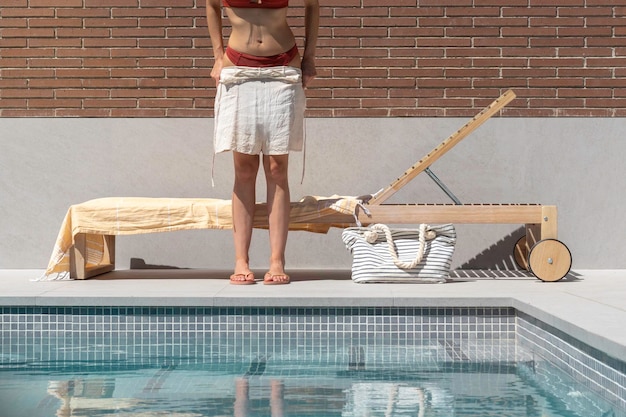 Unrecognizable woman undressing herself when arriving to the\
swimming pool area in a gay and brick background