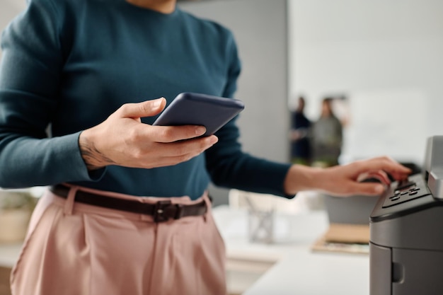 Photo unrecognizable woman using smartphone while printing document