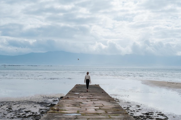 Unrecognizable woman walking on a dike near the calm sea Concept Relaxation disconnection happiness