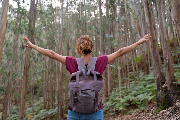 Unrecognizable woman with arms open in a eucalyptus forest. Horizontal view of backpacker female traveling in mountains. People and travel destination concept.