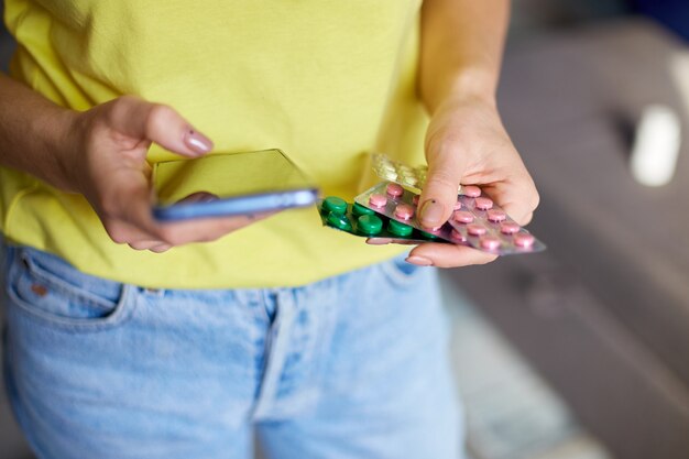 Unrecognizable woman with blister pack of pills and smartphone in hand using online pharmacy store