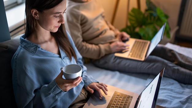 Unrecognizable young couple using laptops on bed indoors, home office in lockdown concept.