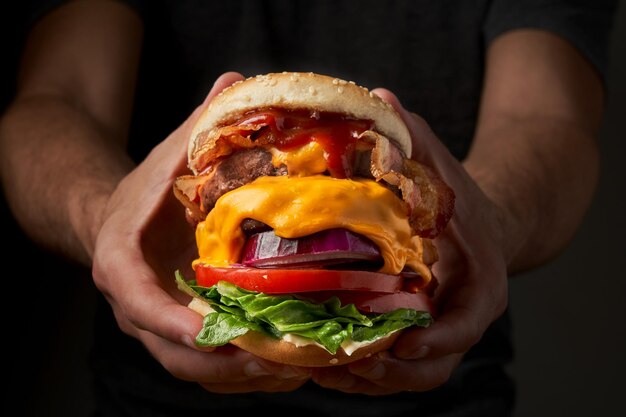 Unrecognizable young man holding in hands fast burger on black\
background