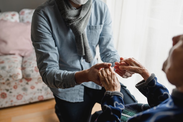 Unrecognizable young man holding hands of old woman. Elderly, care, family concept.