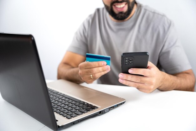 Unrecognizable young man with computer and holding card and cell phone to shop online from home concept shopping black friday cyber monday sales christmas