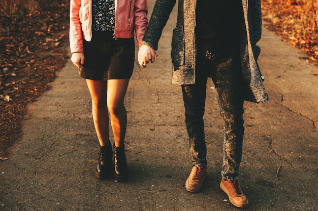 Photo unrecognizable young man and woman holding hands and walking along asphalt countryside road on autumn day.crop couple walking on countryside road