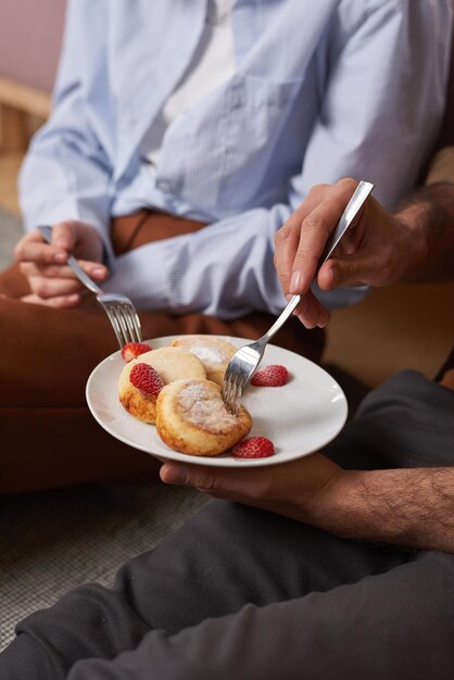 Unrecognizable young man and woman sitting on floor at home having sweet breakfast together