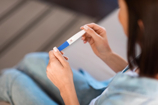 unrecognizable young woman examines positive pregnancy test result sitting indoors