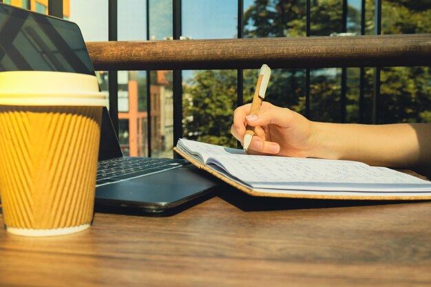 Unrecognizable young woman study at wooden table in shopping mall food court drinking coffee from