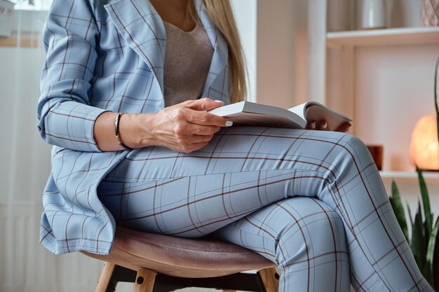 Unrecognizable young woman in a suit reading a book sitting on a chair