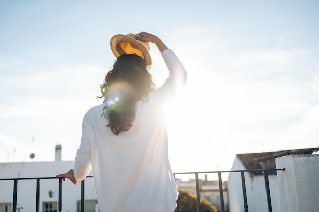 Unrecognizable young woman taking off her hat on a sunny day on the rooftop