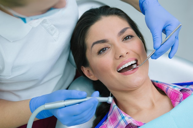 Dentista non riconosciuto che mette uno specchio per la bocca sotto i denti di una paziente calma