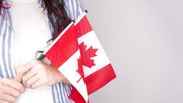 Unrecognized girl student in white blue shirt holding small canadian flag over gray Canada day