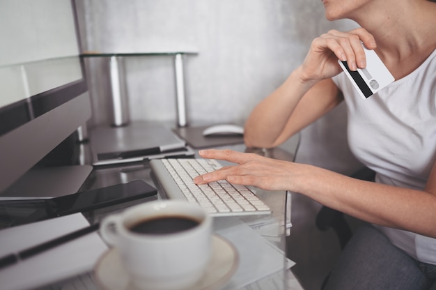 認識できない女性がクレジットカードを手で押し、ラップトップコンピューターのキーボードを使用しています。実業家や起業家が働いています。オンラインショッピング、eコマース、インターネットバンキング、お金の概念を使う
